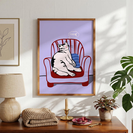 May include: A framed art print featuring a relaxed cat sitting in a red armchair with a blue pillow. The cat is white with black markings. A thought bubble with a fishbone floats above the cat's head. The background is a light purple.