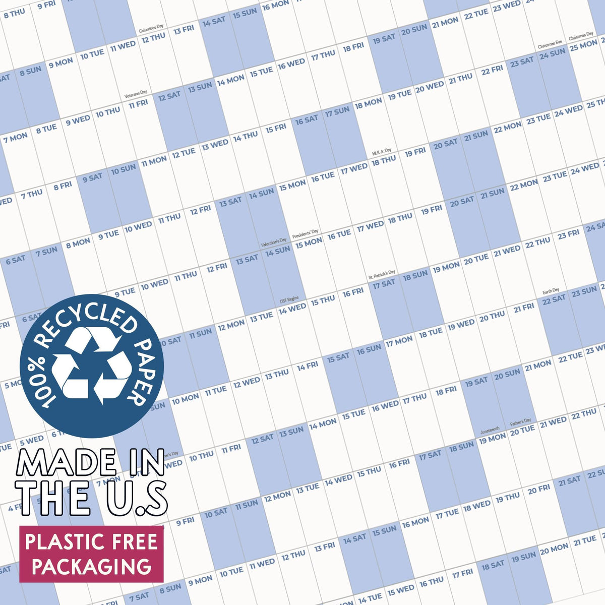May include: A wall calendar featuring a grid layout with alternating white and light blue columns for days of the month. A circular blue badge states 100% RECYCLED PAPER, MADE IN THE U.S, and PLASTIC FREE PACKAGING in white and black text.