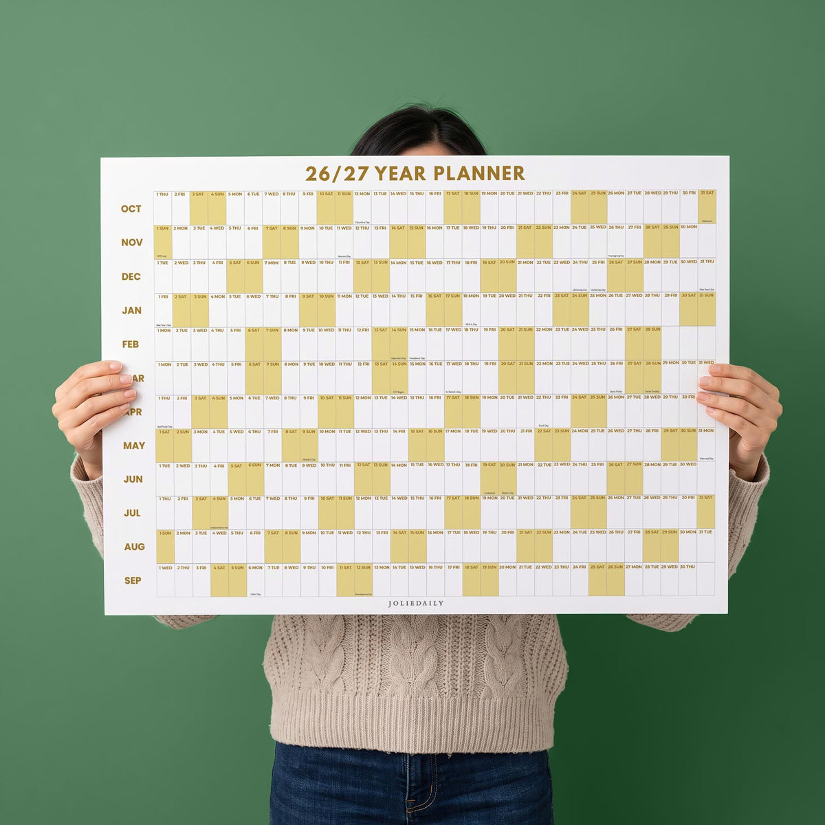 May include: A white wall calendar titled 26/27 YEAR PLANNER with gold text. The grid features rows for months from October to September, with alternating white and gold columns representing days. The bottom center includes the brand name JOLIEDAILY.