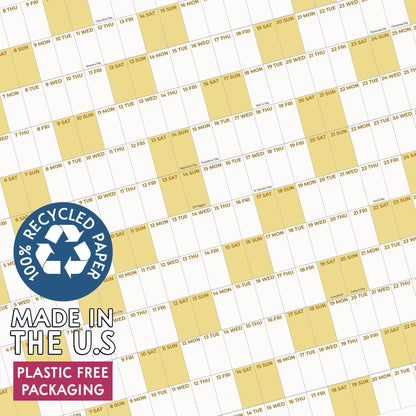 May include: A wall calendar featuring a grid of white and light yellow columns with printed dates and days of the week. A blue circular badge displays the text 100% RECYCLED PAPER, MADE IN THE U.S, and PLASTIC FREE PACKAGING in white font.