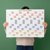 May include: A 26/27 year planner wall calendar featuring a grid layout with months from October to September. The design includes alternating colored blocks in shades of peach, gray, blue, and yellow, with the text JOLIEDAILY at the bottom.