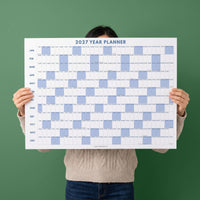May include: A 2027 year planner wall calendar featuring a horizontal grid layout with months listed vertically on the left side. The design uses a white background with dark blue text and light blue shaded blocks for weekends across the entire year.
