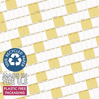 May include: A wall calendar featuring a grid of white and pale yellow alternating columns with printed dates and days of the week. A blue circular badge displays the text 100% RECYCLED PAPER, MADE IN THE U.S, and PLASTIC FREE PACKAGING.