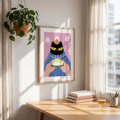 May include: A framed art print featuring a black cat wearing a blue jacket and a party hat, holding a small cake with lit candles. The background is pink with white clouds. The artwork is displayed on a wall near a window.
