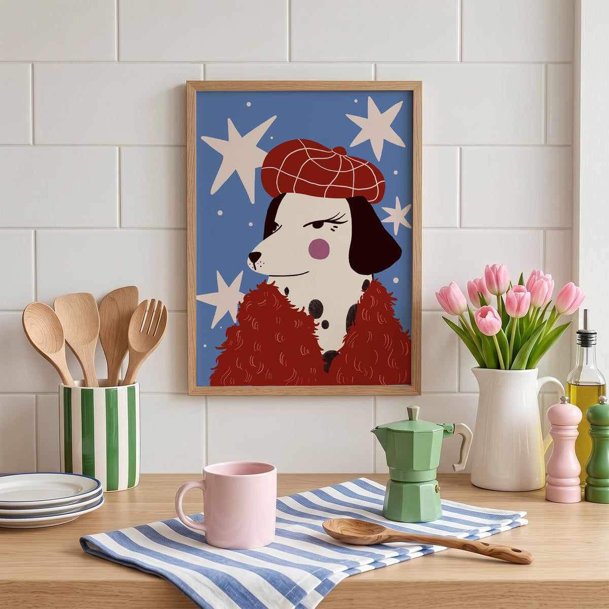 May include: A framed art print featuring a Dalmatian dog wearing a red beret and a red fluffy coat, set against a blue background with white star shapes. The print is displayed on a wooden surface with kitchen items.