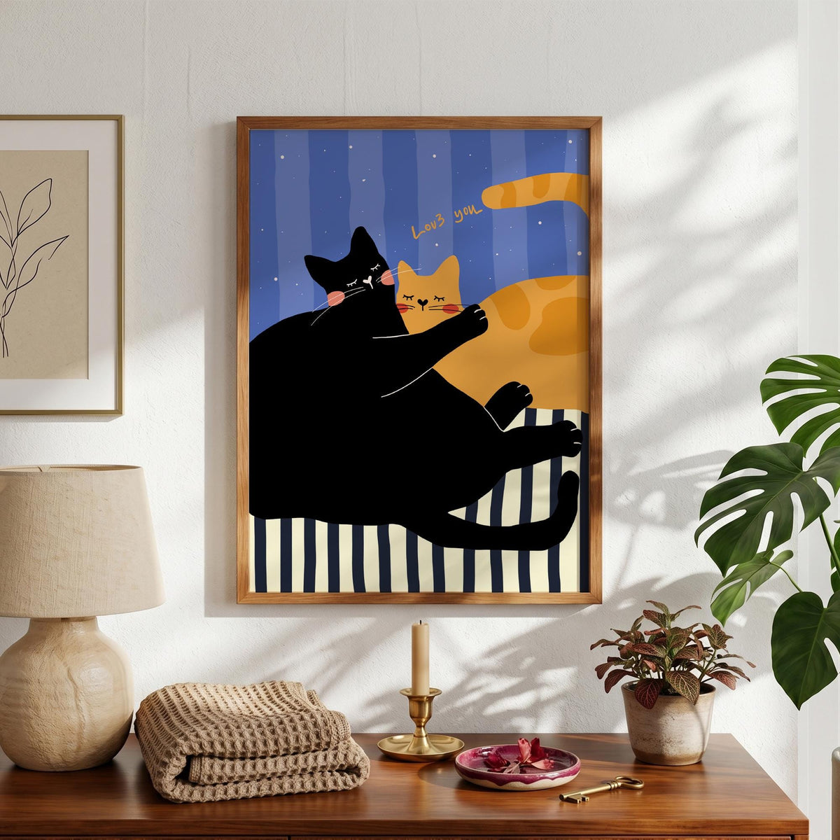May include: A framed art print featuring two cartoon cats. One black cat is embracing an orange cat. The background has blue vertical stripes. The words "Love you" are written above the cats. The print is in a wooden frame.