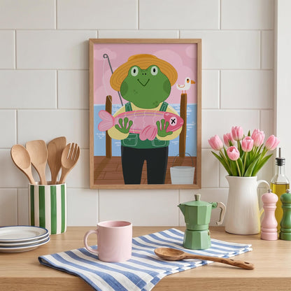 May include: A framed print featuring a cartoon frog wearing a straw hat and overalls, holding a pink fish. The frog is standing on a pier with a fishing rod. A white bucket and a seagull are also visible.