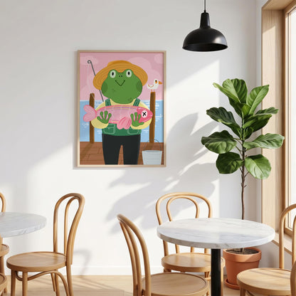May include: A framed illustration depicts a green frog wearing a straw hat and overalls, holding a pink fish. The frog stands on a wooden dock with a fishing rod, a bucket, and a seagull. The background is a pink sky and blue water.