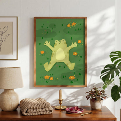 May include: A framed art print featuring a light green frog lying on its back in a field of green grass with orange flowers. The frog has its arms and legs spread out. The artwork is in a wooden frame.