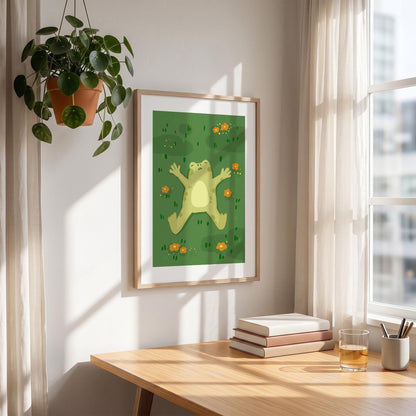 May include: A framed art print featuring a cartoon frog lying on its back in a field of green grass and orange flowers. The frog is light green with a yellow belly. The artwork is displayed on a wooden desk with books and a glass of liquid.