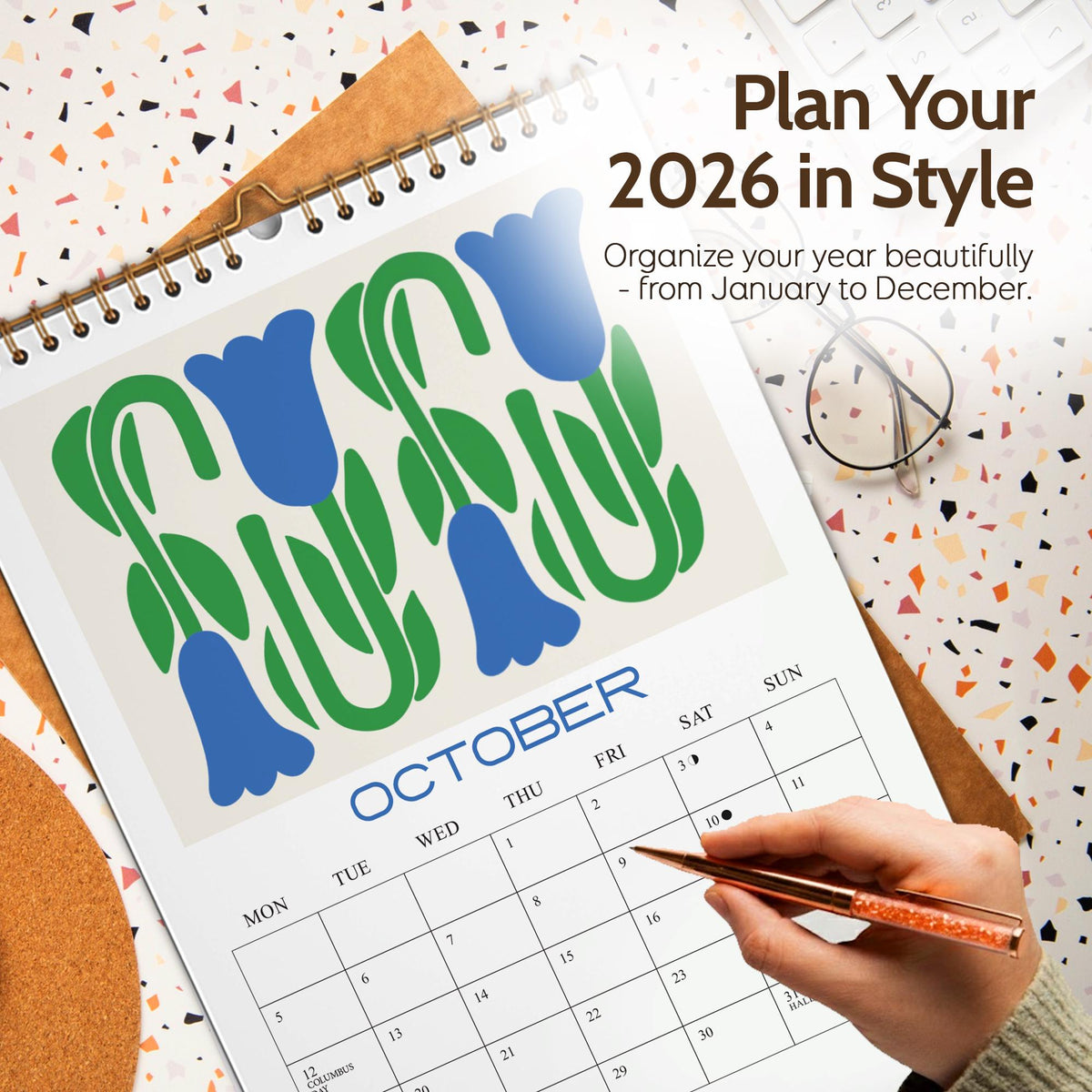 May include: A 2026 wall calendar with a floral design in blue and green. The calendar is open to October, with the text "Plan Your 2026 in Style" at the top. A hand is holding a pen over the calendar.