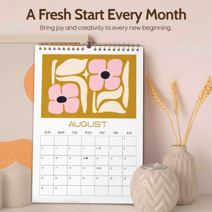May include: A wall calendar for August with a floral design in pink and cream on a mustard yellow background. The calendar is spiral-bound and features the text "A Fresh Start Every Month" and "Bring joy and creativity to every new beginning."
