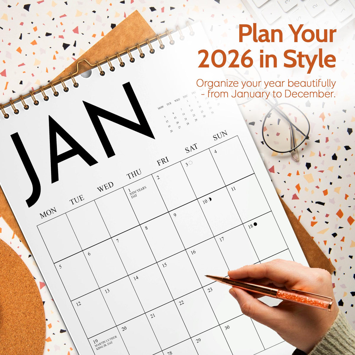 May include: A large, open calendar for January 2026, with a spiral binding and a brown backing. The calendar is open to the first month, with the word "JAN" in large, bold black letters. The text "Plan Your 2026 in Style" is also visible.