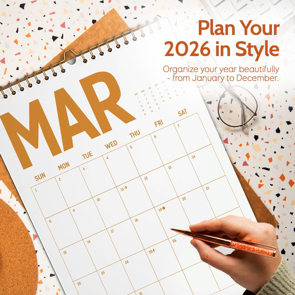 May include: A large, open calendar for March 2026, with the word "MAR" in large, gold letters. The calendar is open to the month of March, with a hand holding a pen. The text "Plan Your 2026 in Style" is visible.