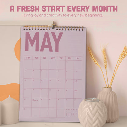 May include: A lavender wall calendar for May with a gold spiral binding. The calendar has a simple grid layout and the word "MAY" in large, bold letters. The text "A FRESH START EVERY MONTH" is at the top. Decorative items include candles and wheat stalks.