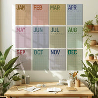 May include: A set of twelve monthly calendars, each with a different pastel color background and the month's name in a coordinating color. The calendars are displayed on a white wall above a wooden desk with plants and office supplies.