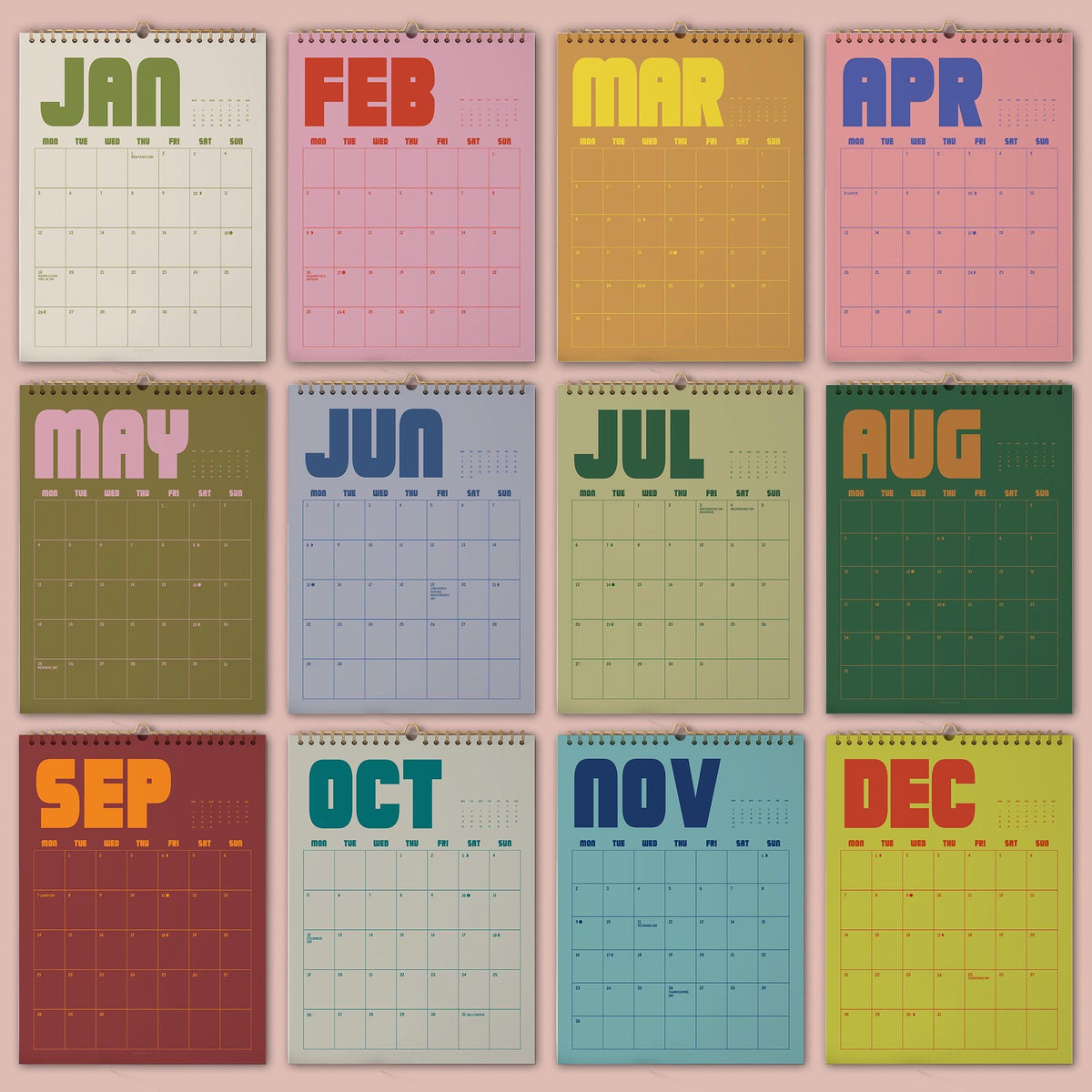 May include: A set of twelve wall calendars, each representing a month of the year. Each calendar features a different color scheme and the month's name in bold, retro-style lettering. The calendars are bound with a metal spiral and have a simple grid layout.