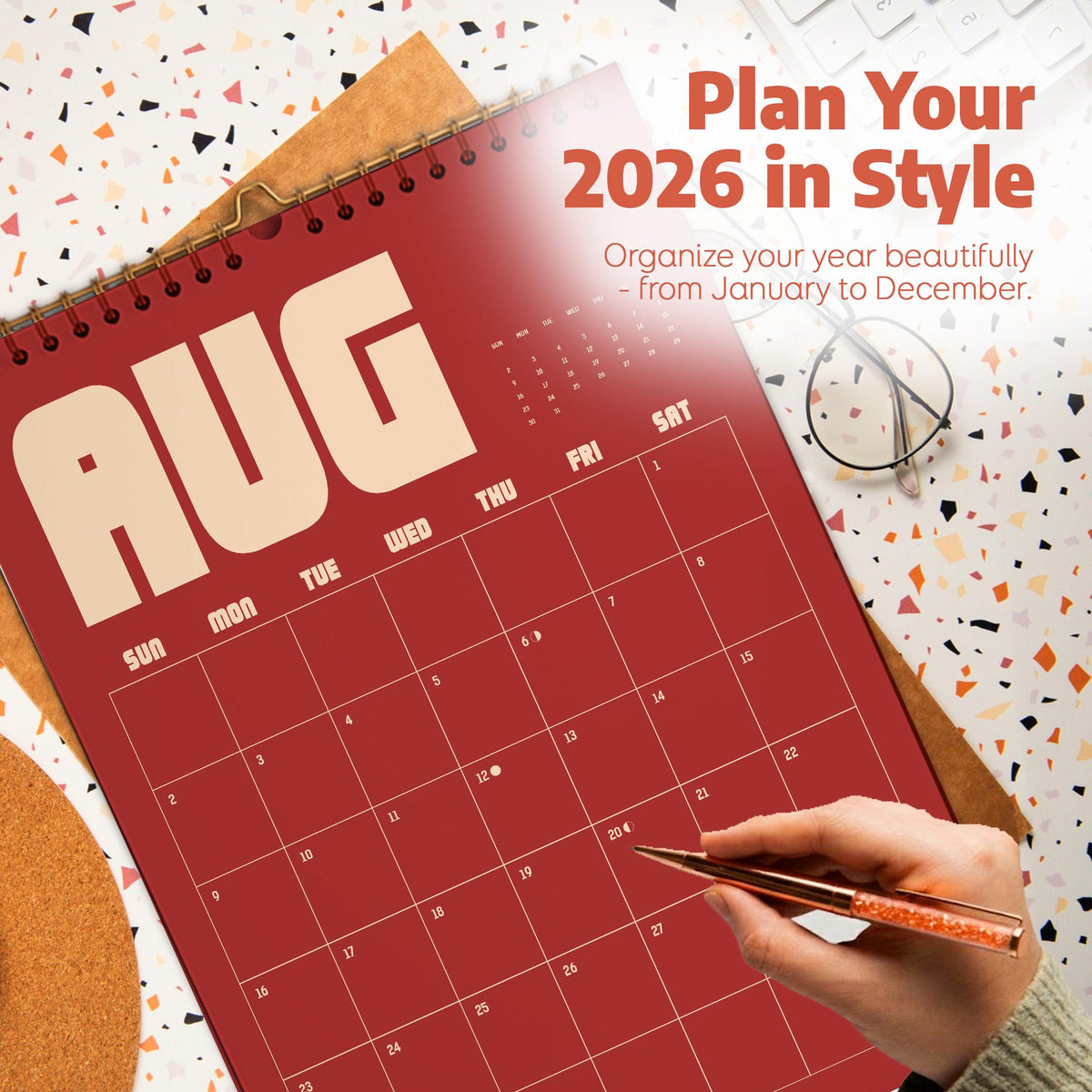 May include: A red 2026 calendar with the month of August displayed. The calendar is open to August, with the days of the week labeled across the top. The text "Plan Your 2026 in Style" is at the top. A hand is holding a pen, ready to write.
