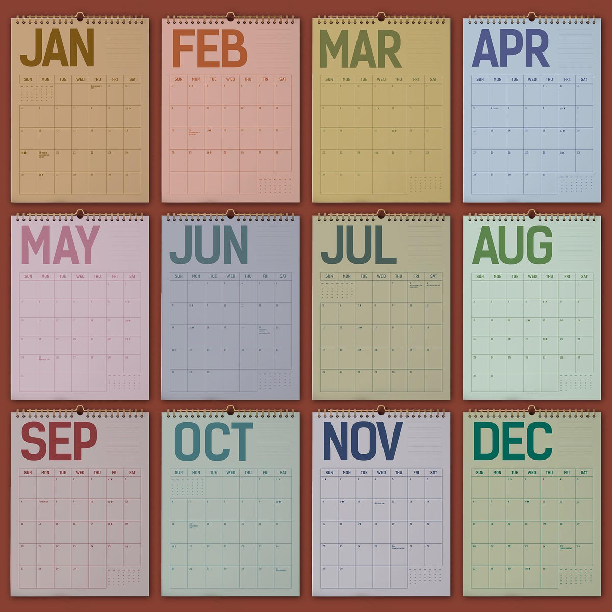 May include: A collection of twelve monthly wall calendars, each with a different color scheme and the month's name at the top. The calendars are arranged in a grid, showcasing the months from January to December. The background is a solid reddish-brown.