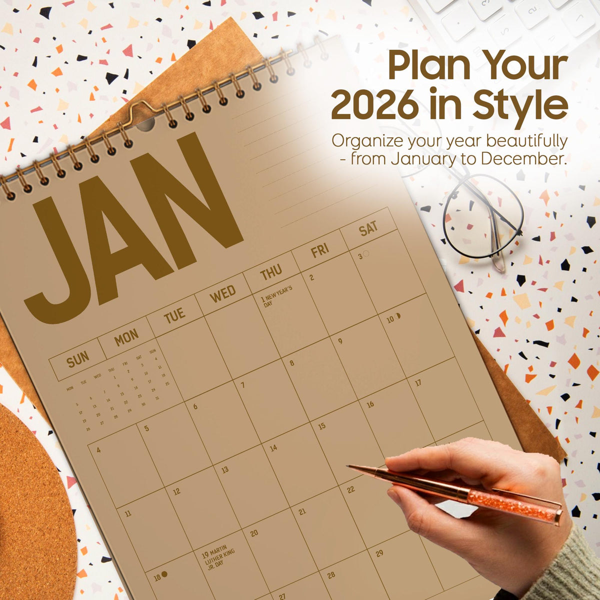 May include: A spiral-bound 2026 calendar open to January, with the word "JAN" in large, gold letters. The calendar is on a patterned surface with the text "Plan Your 2026 in Style" and "Organize your year beautifully - from January to December."