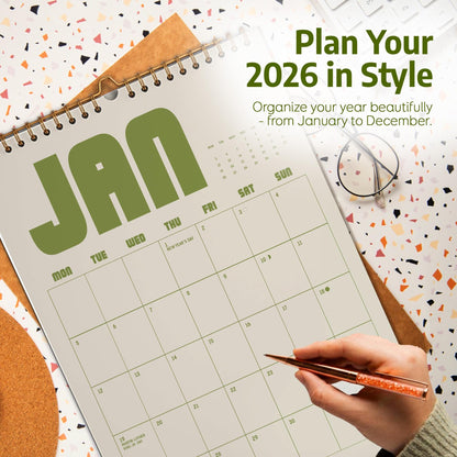 May include: A 2026 wall calendar open to January, with the word "JAN" in large green letters. The calendar is on a desk with a pen, glasses, and the text "Plan Your 2026 in Style". The calendar is designed to organize the year from January to December.