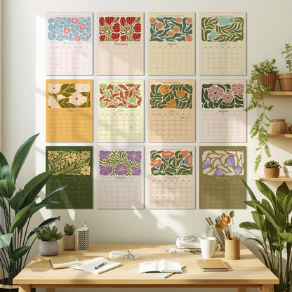 May include: A collection of twelve monthly calendars, each featuring a unique floral design in various colors. The calendars are arranged on a white wall above a wooden desk with plants and office supplies. Each calendar displays the month's name.