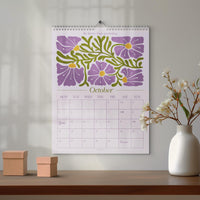 May include: A wall calendar for October with a floral design in purple and green. The calendar has a spiral binding and is hanging on a wall. The text "Be better than yesterday" is at the top.