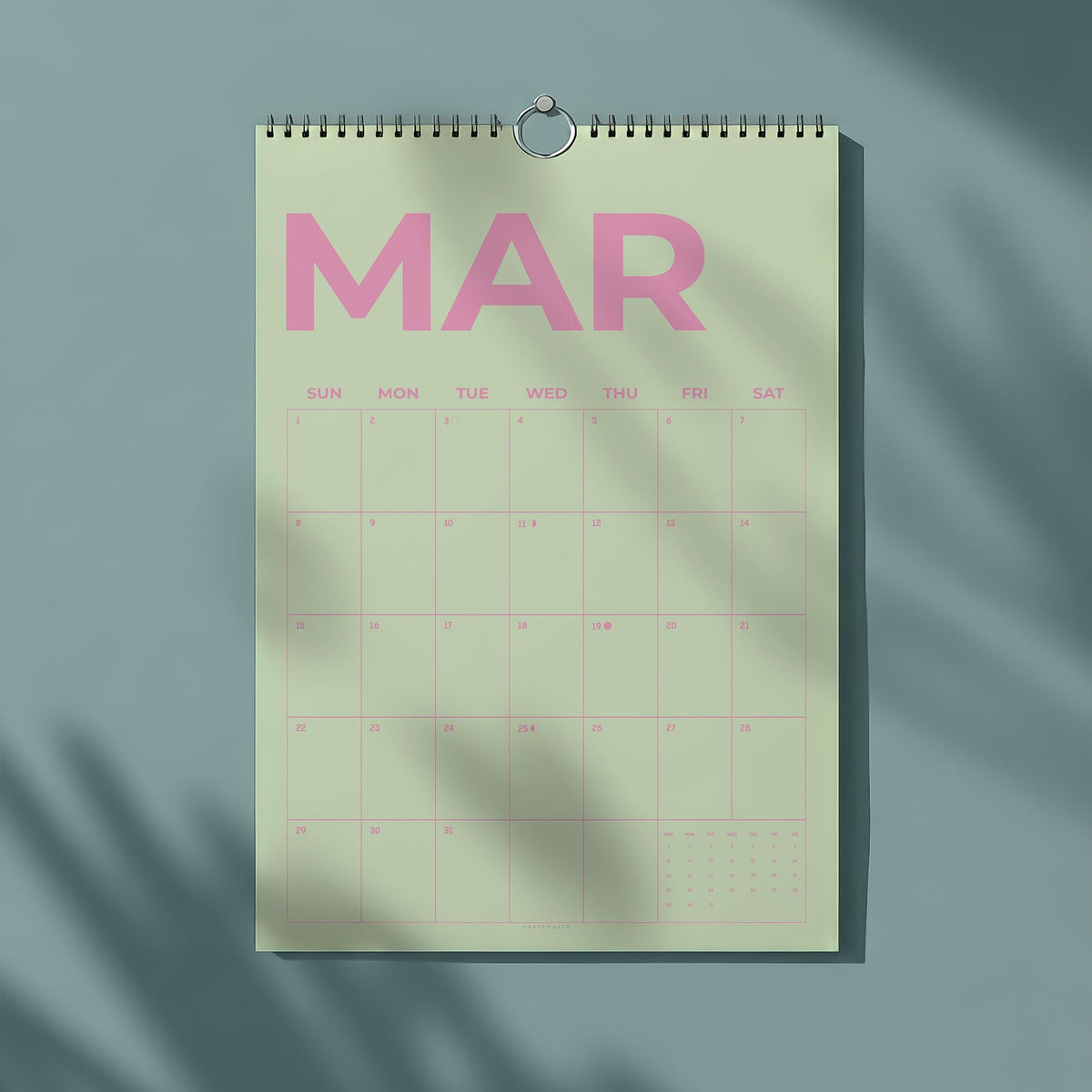 May include: A wall calendar for March, featuring a light green background with pink text. The word "MAR" is prominently displayed at the top, with days of the week and dates below. A silver metal ring holds the calendar.