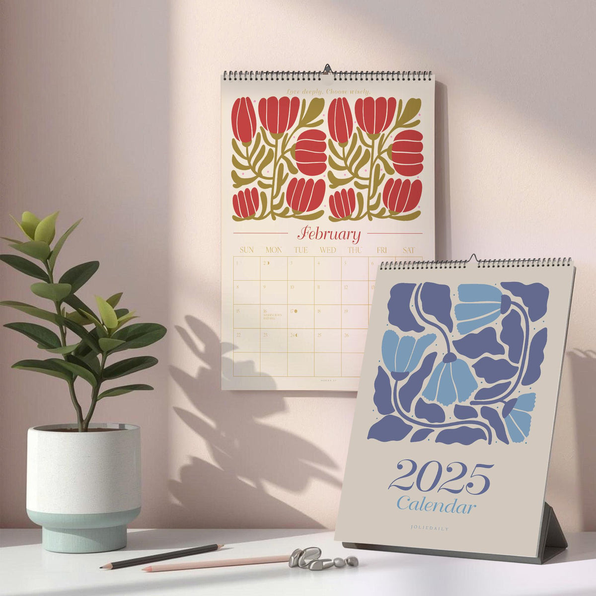 May include: Two calendars, one hanging and one standing, with floral designs. The hanging calendar shows a red floral pattern with the month of February. The standing calendar displays a blue floral design and the text "2025 Calendar".