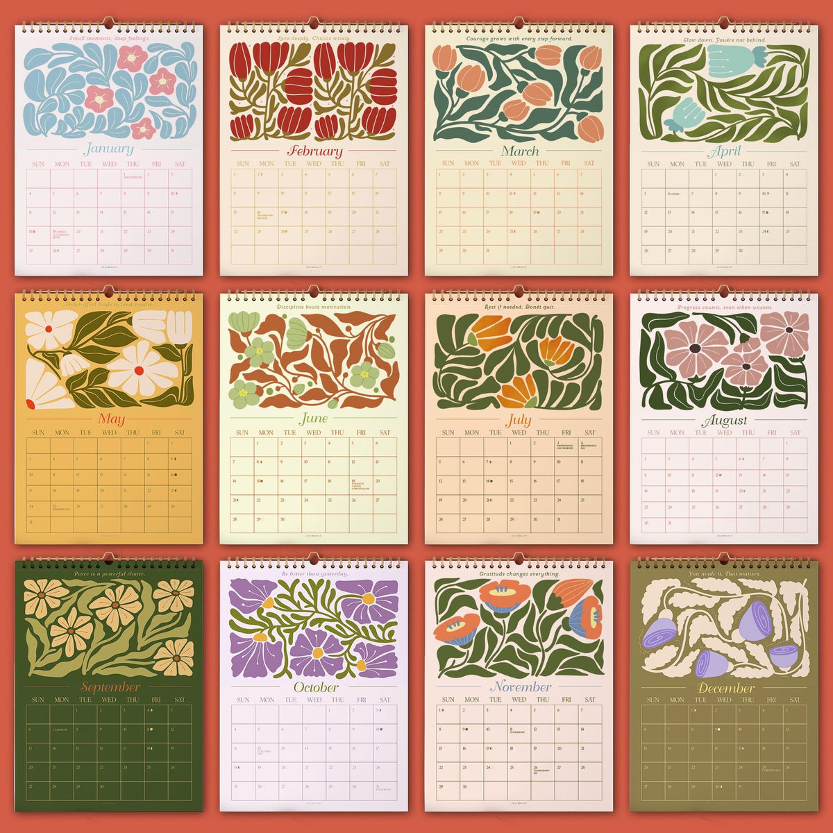 May include: A set of twelve monthly wall calendars. Each calendar features a different floral design in a variety of colors, including blue, red, orange, and purple. The months are labeled in a simple font. The calendars are bound with a metal spiral.