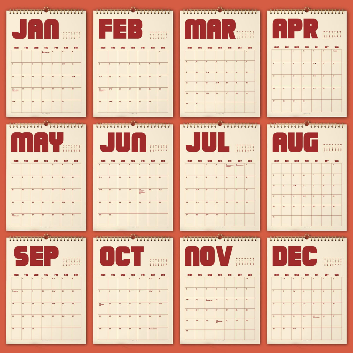 May include: A collection of twelve monthly wall calendars, each displaying a different month from January to December. The calendars have a cream-colored background with red text and a spiral binding at the top. The months are printed in bold, uppercase letters.