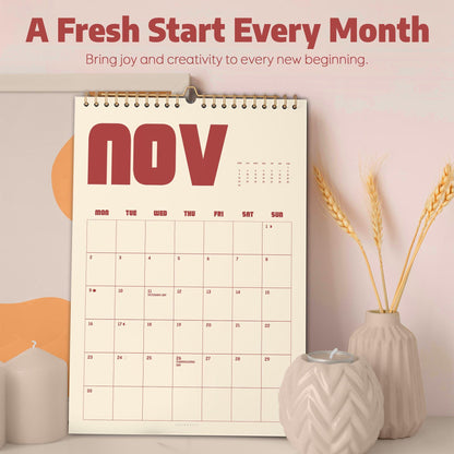 May include: A wall calendar for November with a gold spiral binding. The calendar has a cream-colored background with red text that reads "NOV". The top of the calendar reads "A Fresh Start Every Month". A vase with wheat stalks and a candle holder are in the foreground.