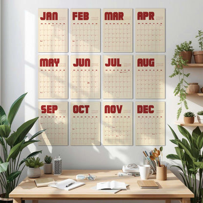 May include: A set of twelve monthly calendars displayed on a white wall. Each calendar features a cream-colored background with a grid of dates and a bold, red month name at the top. The calendars are arranged in three rows of four.