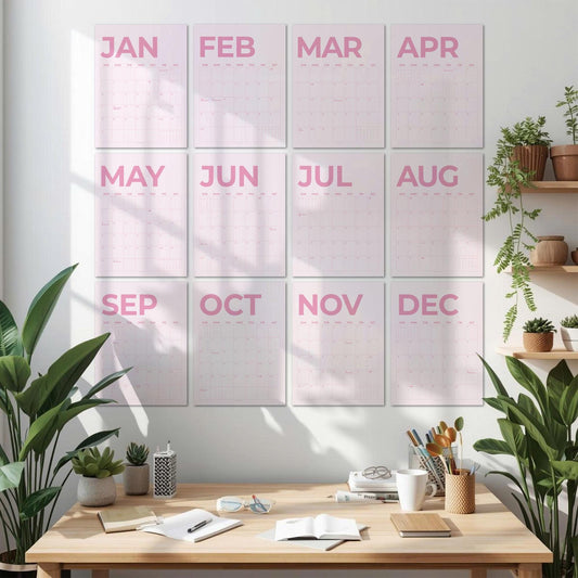 May include: A wall calendar set featuring twelve individual rectangular sheets, each displaying a month from January to December in bold pink lettering. The calendar pages are arranged in a grid of three columns and four rows on a white wall.