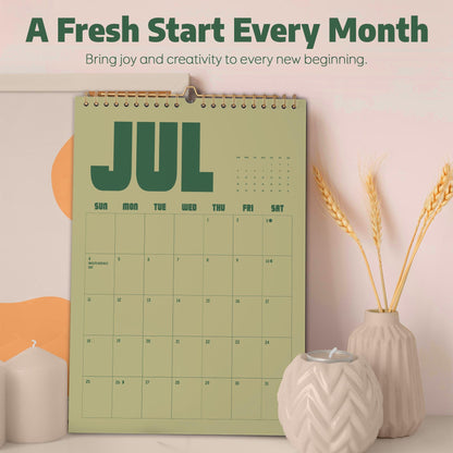 May include: A wall calendar with a sage green background and dark green text displaying the month of July. The calendar features a grid layout for dates, a spiral binding at the top, and the printed text A Fresh Start Every Month.