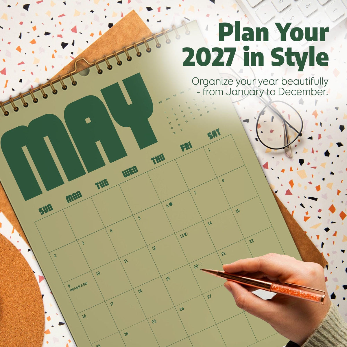 May include: A wall calendar for May 2027 with a sage green background and dark green text. The calendar features a grid layout for the month, wire-o binding at the top, and the printed text Plan Your 2027 in Style and Organize your year beautifully.