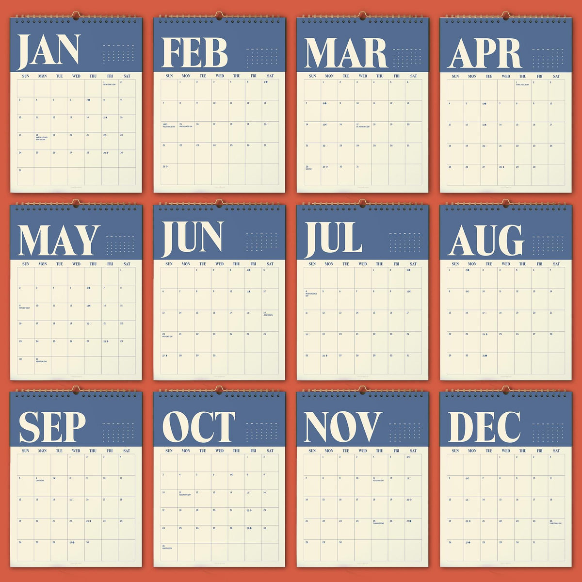 May include: A twelve-month wall calendar featuring a blue header for each month with white serif lettering for the month names. Each page displays a grid for the days of the week, starting with Sunday, against a cream-colored background.