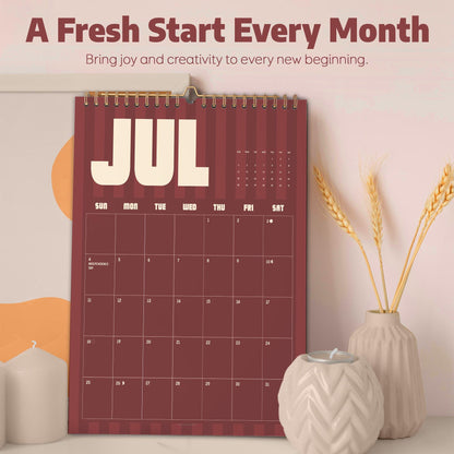 May include: A wall calendar for the month of July featuring a dark red background with vertical stripes and cream-colored text. The calendar displays the text A Fresh Start Every Month and Bring joy and creativity to every new beginning.