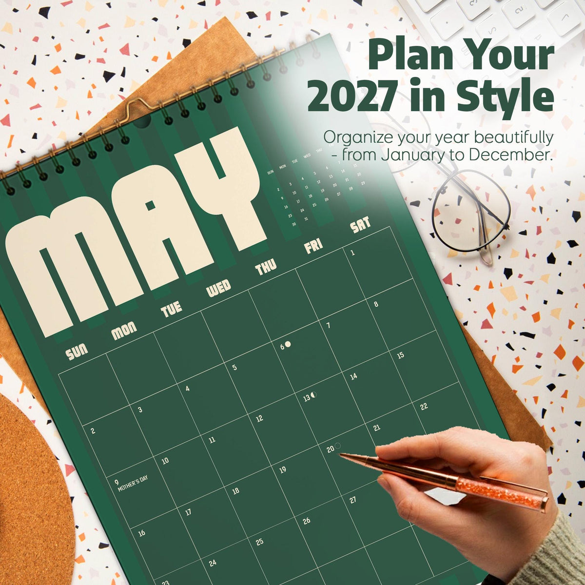 May include: A 2027 wall calendar featuring a dark green background with vertical stripes and large cream-colored text reading MAY. The calendar grid displays days of the week and dates, with text stating Plan Your 2027 in Style and Organize your year beautifully.