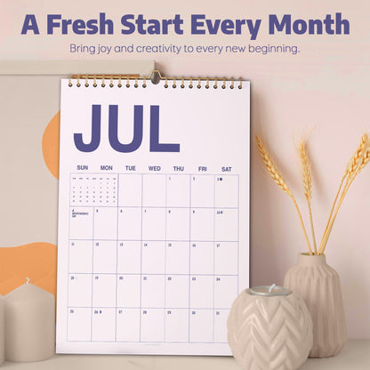 May include: A wall calendar for the month of July with a white background, dark blue text, and a gold spiral binding. The text reads A Fresh Start Every Month, Bring joy and creativity to every new beginning, and JUL. The grid shows days of the week.