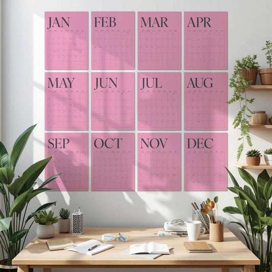 May include: A wall calendar set featuring twelve individual pink rectangular sheets, each labeled with a month from January to December in dark gray text. Each sheet contains a grid for dates, displayed in a clean, organized layout on a white wall.