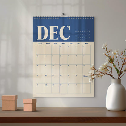 May include: A wall calendar for the month of December featuring a dark blue header with the text DEC in large cream letters. The grid below is cream-colored with dark blue text for the days of the week and dates, including the label Christmas on the 25th.