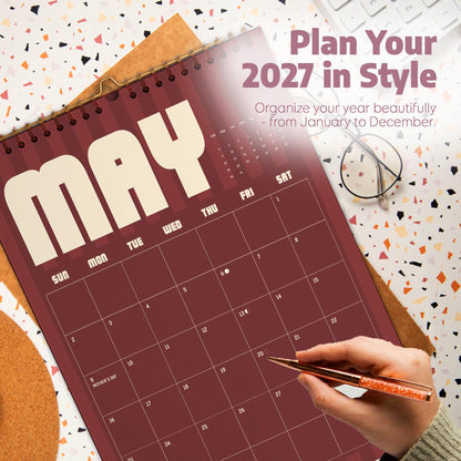 May include: A wall calendar for May 2027 with a dark red background and cream-colored text. The calendar features a grid layout with days of the week and dates. Text on the calendar reads: Plan Your 2027 in Style, Organize your year beautifully, and MAY.