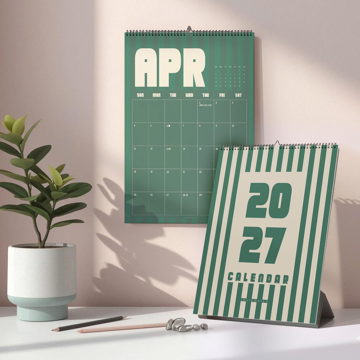 May include: A wall calendar displaying the month of April and a desk calendar featuring the year 2027. Both calendars have a green and cream striped design. The wall calendar shows a grid for April, while the desk calendar displays the year 2027.