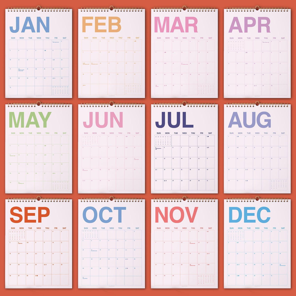 May include: A wall calendar featuring twelve individual pages, one for each month of the year. Each page displays the month name in a distinct pastel color at the top, followed by a grid of days with thin black lines on a white background.