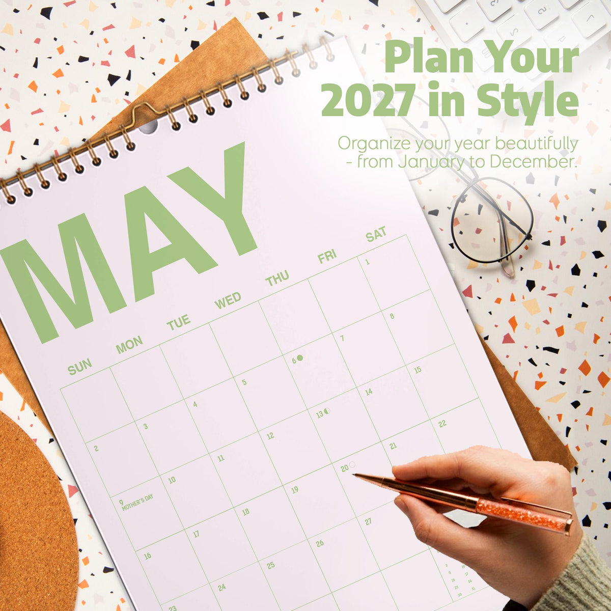 May include: A 2027 wall calendar with a spiral binding, featuring the month of May in large green letters. The text reads Plan Your 2027 in Style and Organize your year beautifully - from January to December. The calendar has a white grid layout.