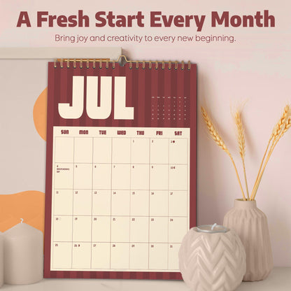 May include: A wall calendar for the month of July featuring a dark red and cream striped background with the text JUL at the top. The calendar grid displays days of the week and dates, including Independence Day on the 4th, with a gold spiral binding.