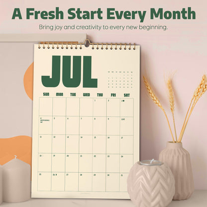 May include: A wall calendar with a cream background and dark green text displaying the month of July. The calendar features a grid layout with days of the week and dates. The text A Fresh Start Every Month and Bring joy and creativity to every new beginning is printed at the top.