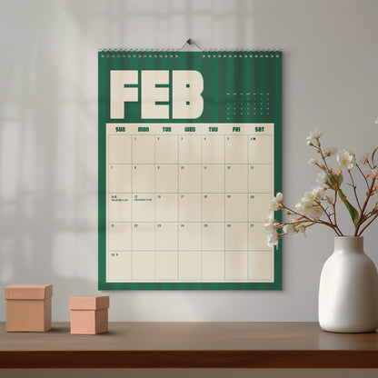 May include: A wall calendar for the month of February featuring a dark green background with vertical stripes. The calendar grid is cream-colored with bold, dark green text. It displays the days of the week and dates, including Valentine's Day.