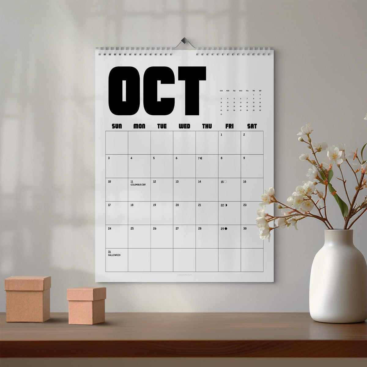 May include: A wall calendar for the month of October featuring a white background with bold black text reading OCT at the top. The grid displays days of the week from Sunday to Saturday with numbered dates, including labels for Columbus Day and Halloween.